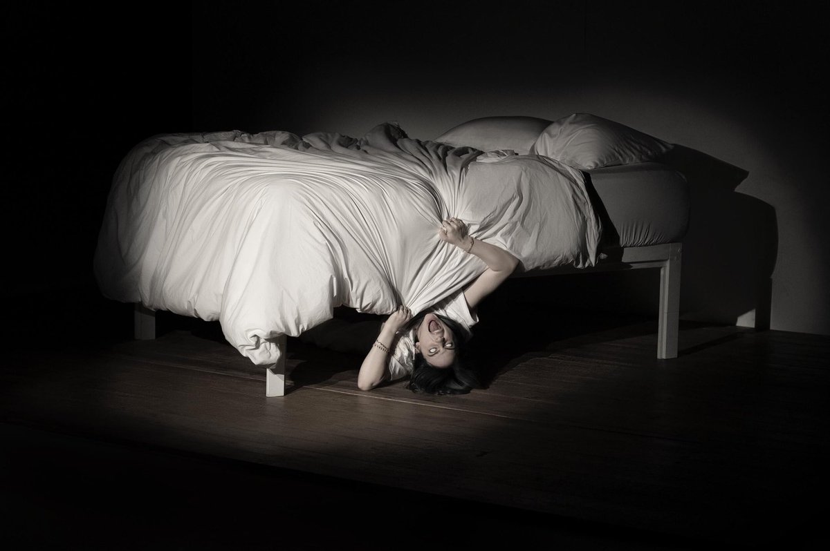 La chanteuse Billie Eilish imitant un monstre en dessous d'un lit