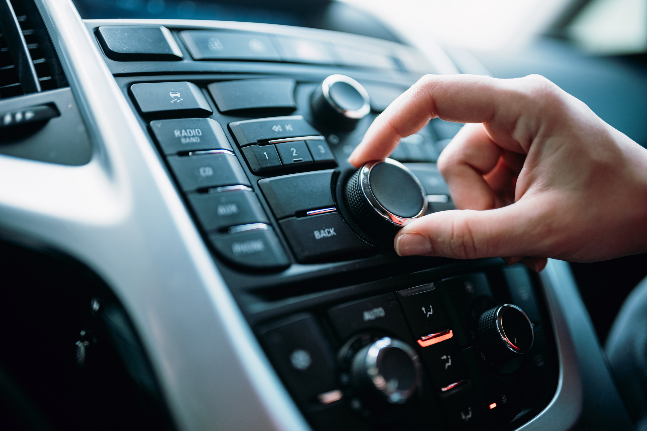 La main d'une jeune femme sur le bouton de volume d'une radio de voiture