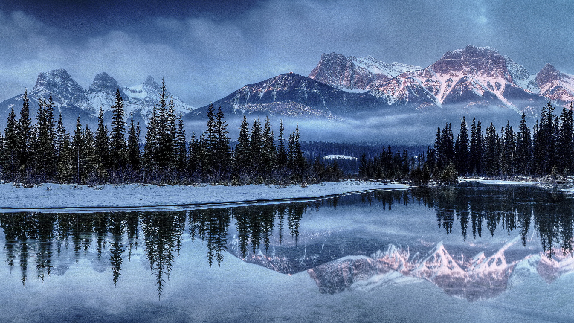 Le paysage d'un lac, de sapins, de montagnes et de nuages en hiver